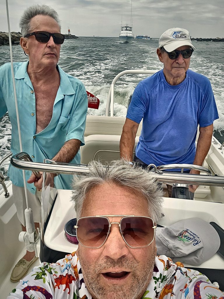 Rick Rude taking a selfie on a boat heading out of Rudee Inlet with friends Carter Turpin and Chuck Kirkwood, the jetties and the Atlantic behind them.