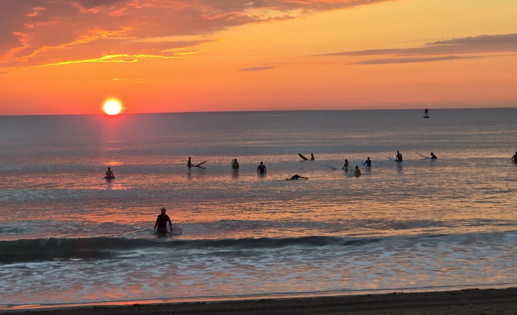 Surfers standing at the water taking in the sunrise at Virginia Beach